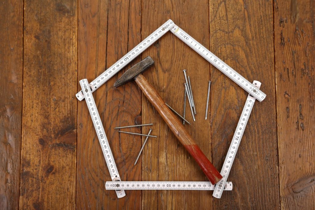 Hammer and nails inside a ruler house shape — remodel vs repair your home