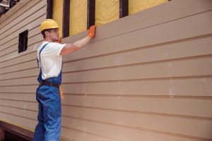 A construction worker installs new siding. The boards are clean and not warped, and the area underneath shows no sign of water damage--siding replacement signs